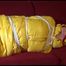 Lucy tied, gagged and hooded on a red sofa wearing an orange venice beach pant and a yellow down jacket (Video)