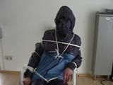 An archive girl tied, gagged and hooded two times on a sofa and chair wearing a shiny blue rainwear (Video)