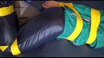 Mara tied, gagged and hooded with tape on a blue sofa wearing an blue/green rain combination (Video)