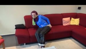 Mara tied and gagged on a sofa wearing a shiny black rain pants and a got lightblue rain jacket (Video) 