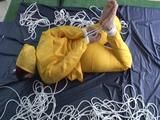Archive girl tied and gagged on bed wearing a shiny yellow rainwear (Video)