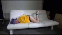 Mara with blue hairs wearing a sexy blue/yellow shiny nylon shorts and a yellow rain jacket tied and gagged with ropes and a ball gag on the sofa (Video)