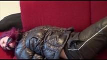 Mara tied and gagged on a sofa wearing a shiny black rain pants and down jacket (Video) 