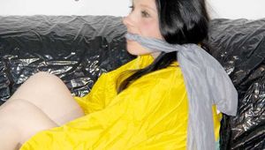 LUCY tied and gagged with ropes and a ballgag on a sofa wearing a sexy black/yellow shiny nylon shorts and a yellow rain jacket (Pics)