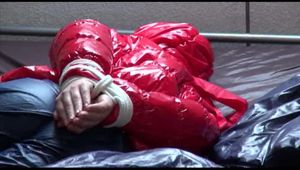 Mara tied, gagged and hooded on bed wearing s shiny red down jacket and a darkblue rain pants (Video)