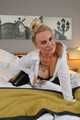 Busty blonde Frida posing in white shirt, leather corsage and black glossy leggins on bed