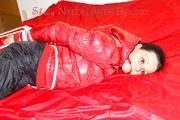 Lucy tied, gagged and hooded on a bed wearing a sexy black shiny nylon pants and a red down jacket (Pics)