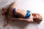 Dolly: cleave-gagged blonde barefoot girl in blue bikini, hog-cuffed with steel handcuffs and legcuffs, rolls and wiggles on the floor