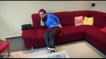 Mara tied, gagged and hooded on a sofa wearing a shiny blue rainjacket and a black rain pants  (Video)