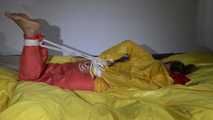 Watching Sandra  wearing an orange shiny nylon rain pants and a yellow shiny nylon rain jacket being tied and gagged on a bed with ropes and a clothgag (Video)
