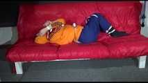 Lucy wearing a blue rain pants and an orange rain jacket being tied and gagged with belts on a sofa (Video)