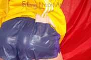 Sonja wearing a sexy blue/purple own designed shiny nylon shorts and a yellow rain jacket posing on the red sofa (Pics)