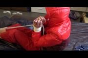 Pia tied and gagged on bed wearing a shiny red down jacket and a red rain pants (Video)