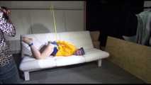 Mara with blue hairs wearing a sexy blue/yellow shiny nylon shorts and a yellow rain jacket tied and gagged with ropes and a ball gag on the sofa (Video)