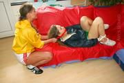 Stella ties and gagges Leonie on a red sofa both wearing sexy shiny nylon shorts and rainjackets (Pics)