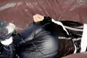 Mara wearing a sexy shiny black rian pants and a sexy shiny black rain jacket tied and gagged with tape and cloth gag on a sofa (Pics)