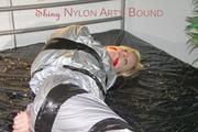 Pia tied and gagged with tape on a bed wearing a sexy silver rainwear combination (Pics) 