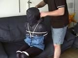 An archive girl tied, gagged and hooded two times on a sofa and chair wearing a shiny blue rainwear (Video)