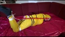 Lucy tied, gagged and hooded on a sofa with dark ropes wearing a sexy yellow rainwear combination (Video)