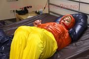 Pia tied and gagged on bed wearing a yellow rain pants and an orange downjacket (Pics)