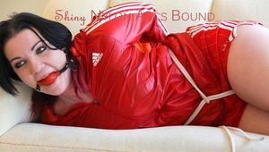 Jill tied and gagged lying on a sofa wearing a sexy shiny red adidas shorts and a red rain jacket (Pics)