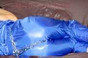 PIA tied and gagged with a pillory on a sofa wearing a sexy blue really shiny nylon rain bib overall (Pics)