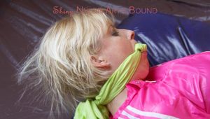 Pia in a green shiny nylon shorts with white stripes and a pink rain jacket tied and gagged in a bed (Pics)