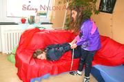 Leonie tied and gagged by Stella on a sofa both wearing sexy shiny nylon rainwear (Pics)