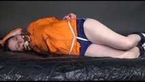 Lucy tied and gagged on a bed wearing a blue shiny nylon shorts and an orange shiny nylon rain jacket (Video)
