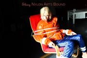 Pia tied and gagged on a chair wearing a shiny orange down jacket and a shiny blue rain pants (Pics)