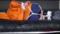 Lucy tied and gagged on a bed wearing a blue shiny nylon shorts and an orange shiny nylon rain jacket (Video)