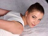 Barefoot Lisa in white tank-top and blue jeans, hogcuffed with steel cuffs, wiggles on the bed