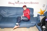 Jill tied, gagged and hooded infront of a sofa wearing a darkblue rain pants and a red rain jacket (Pics)