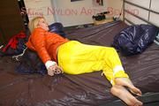 Pia tied and gagged on bed wearing a yellow rain pants and an orange downjacket (Pics)