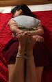 Ballgagged barefoot Lois in grey t-shirt and red skirt, hogtied with hemp rope, rolls and wiggles on the mattress