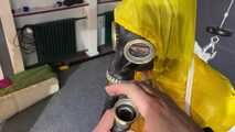 See Lady M, bound in shiny yellow Rainsuit, wearing a latex Mask and a Gasmask
