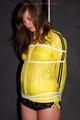 Alina tied and gagged to a pole in nylon shorts and yellow cagoule