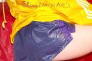 Sonja wearing a sexy blue/purple own designed shiny nylon shorts and a yellow rain jacket posing on the red sofa (Pics)
