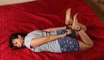 Ballgegged barefoot Lois in t-shirt and shorts, hog-cuffed on the floor with hinged cuffs, wiggles helplessly