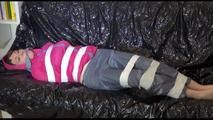 Mara tied and gagged with tape on a blue sofa wearing a supersexy pink/grey rainwear combination (Video)