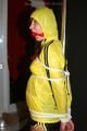 Alina tied and gagged to a pole in nylon shorts and yellow cagoule