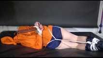 Lucy tied and gagged on a bed wearing a blue shiny nylon shorts and an orange shiny nylon rain jacket (Video)
