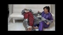 Sophie tied and gagged by Jill on a sofa wearing a shiny silver PVC sauna suit which is slitted by Jill (Video)