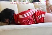 Jill tied and gagged lying on a sofa wearing a sexy shiny red adidas shorts and a red rain jacket (Pics)