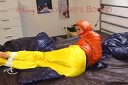 Pia tied and gagged on bed wearing a yellow rain pants and an orange downjacket (Pics)