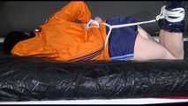 Lucy tied and gagged on a bed wearing a blue shiny nylon shorts and an orange shiny nylon rain jacket (Video)
