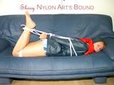 Leonie tied, gagged and hooded sitting on a sofa wearing a sexy shiny nylon shorts and a rain jacket (Pics)
