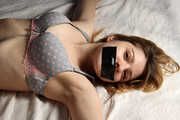 Barefoot tapegagged Grace in grey lace polka dot bra and panties, tied on the bed with her hands and legs wide-spread, wiggles helplessly