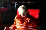 Pia tied and gagged on a chair wearing a shiny orange down jacket and a shiny blue rain pants (Pics)