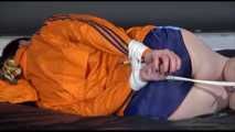 Lucy tied and gagged on a bed wearing a blue shiny nylon shorts and an orange shiny nylon rain jacket (Video)